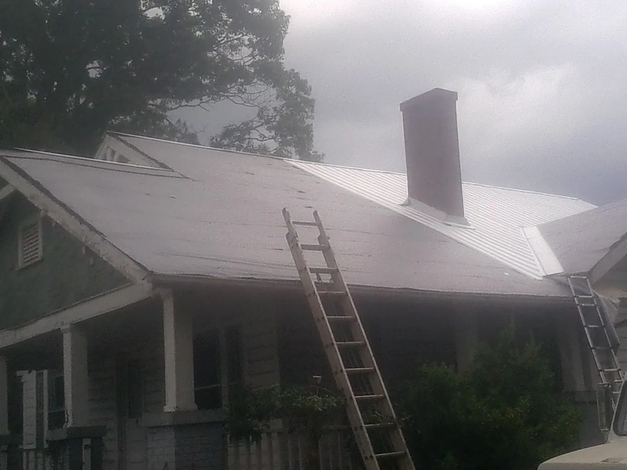 Ladders against a metal roof on an older home with a brick chimney in Windsor